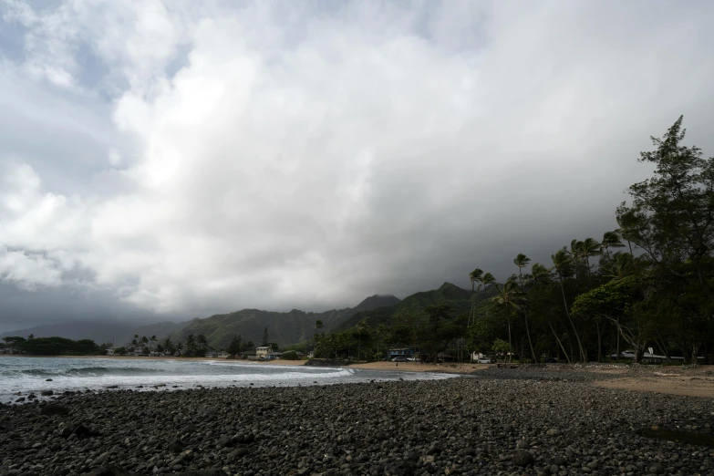 the sky above a beach and tree covered shore