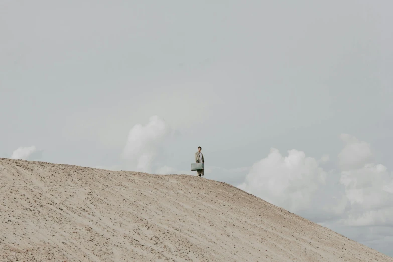 man walking in sand area with gray sky above