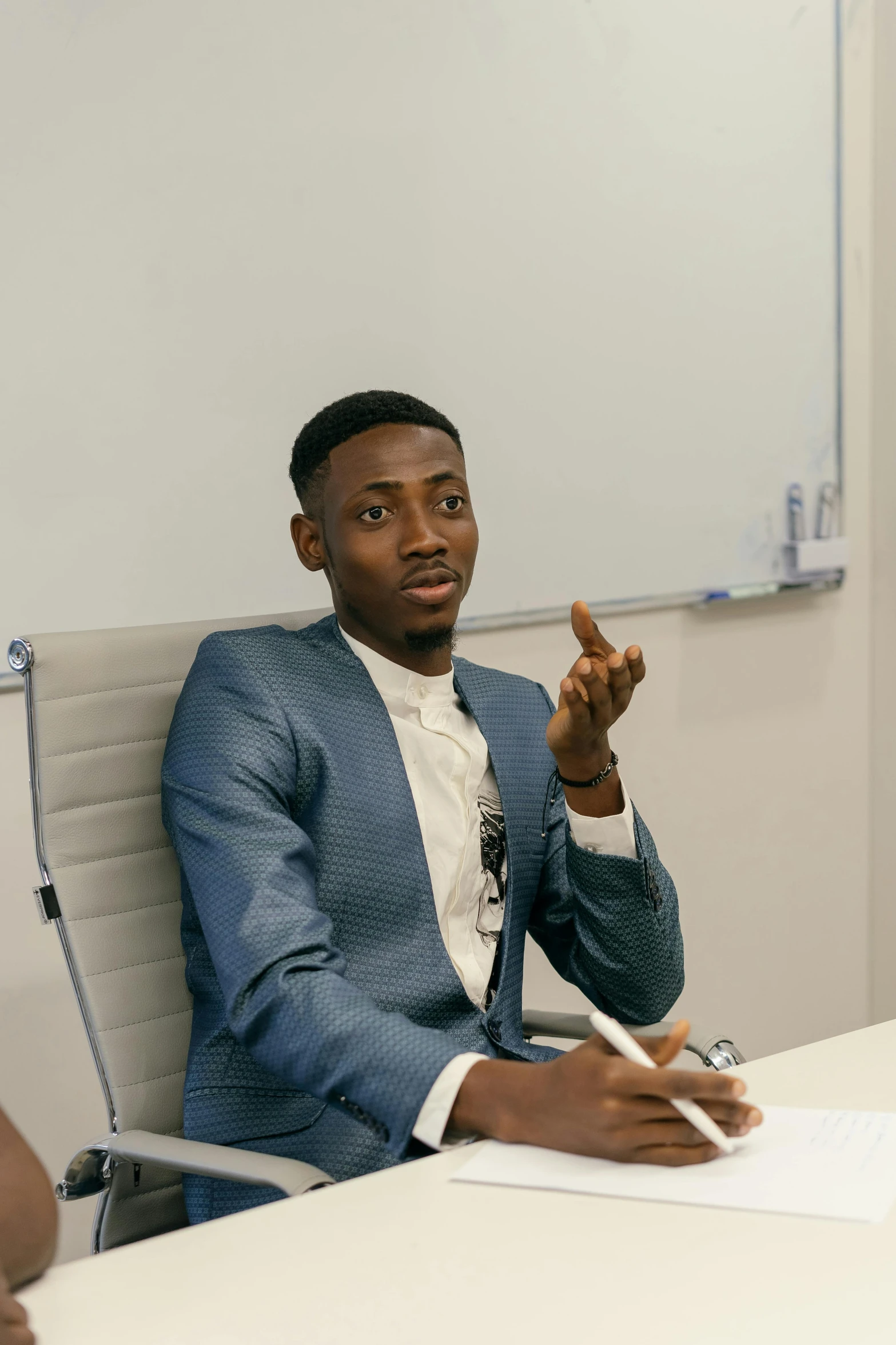 a man in a suit at a conference room table giving the peace sign