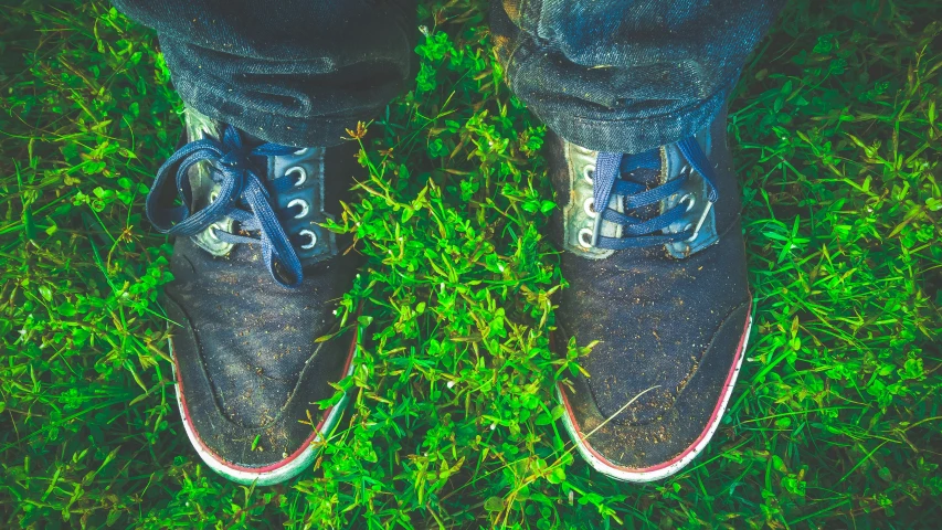 a man wearing blue sneakers standing on some grass