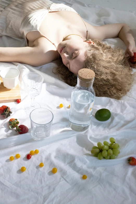 a woman lying on a bed next to fruit and water