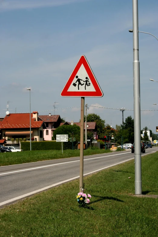 a caution sign on the side of a street near a grass area