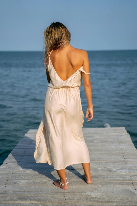 the back of a woman walking on a dock over looking the ocean
