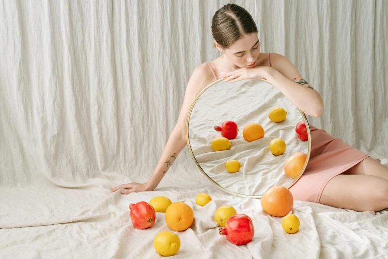 a woman in a white shirt holding a mirror and a bunch of fruit
