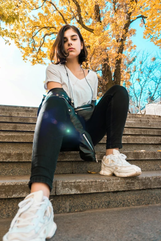 the girl sits on steps wearing headphones and using her phone