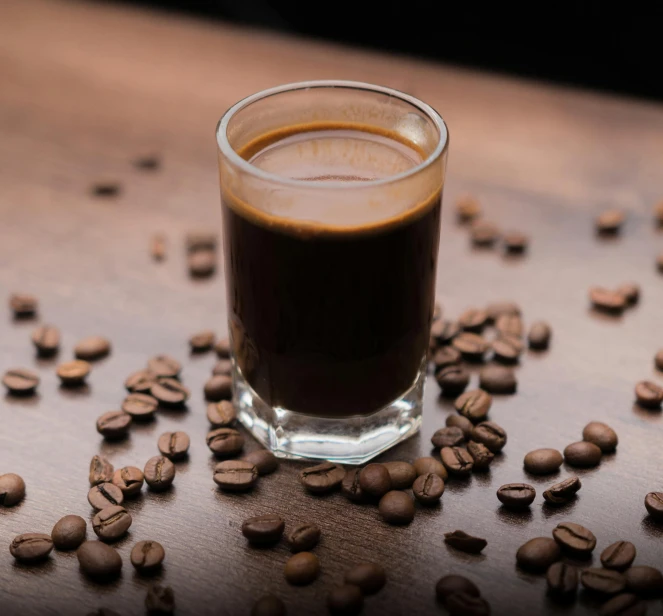 a s glass with liquid on the table with some coffee beans