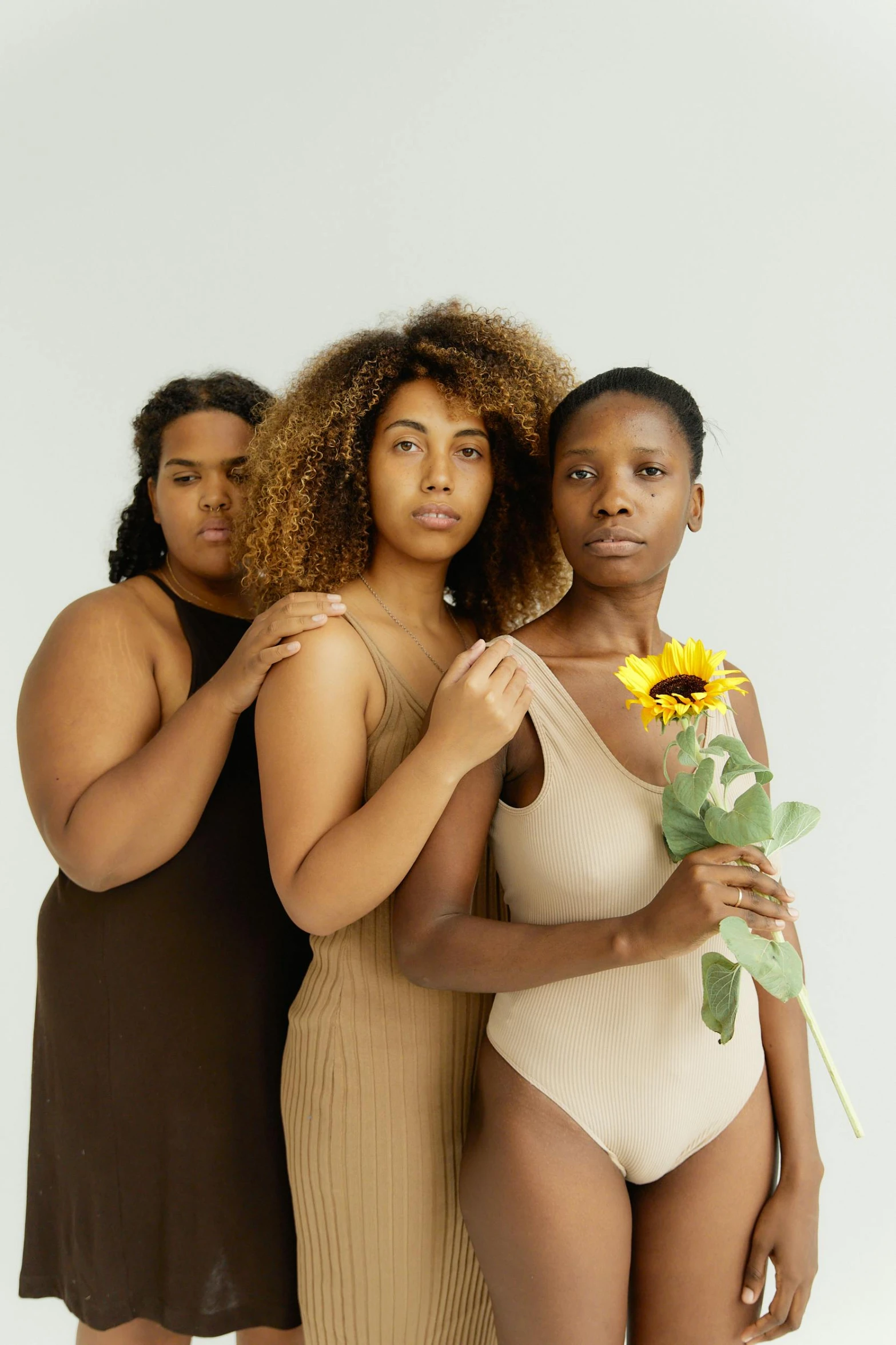 three young women in matching swimsuits pose with one holding a sunflower