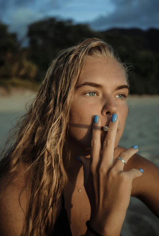 a beautiful young woman standing on the beach smoking