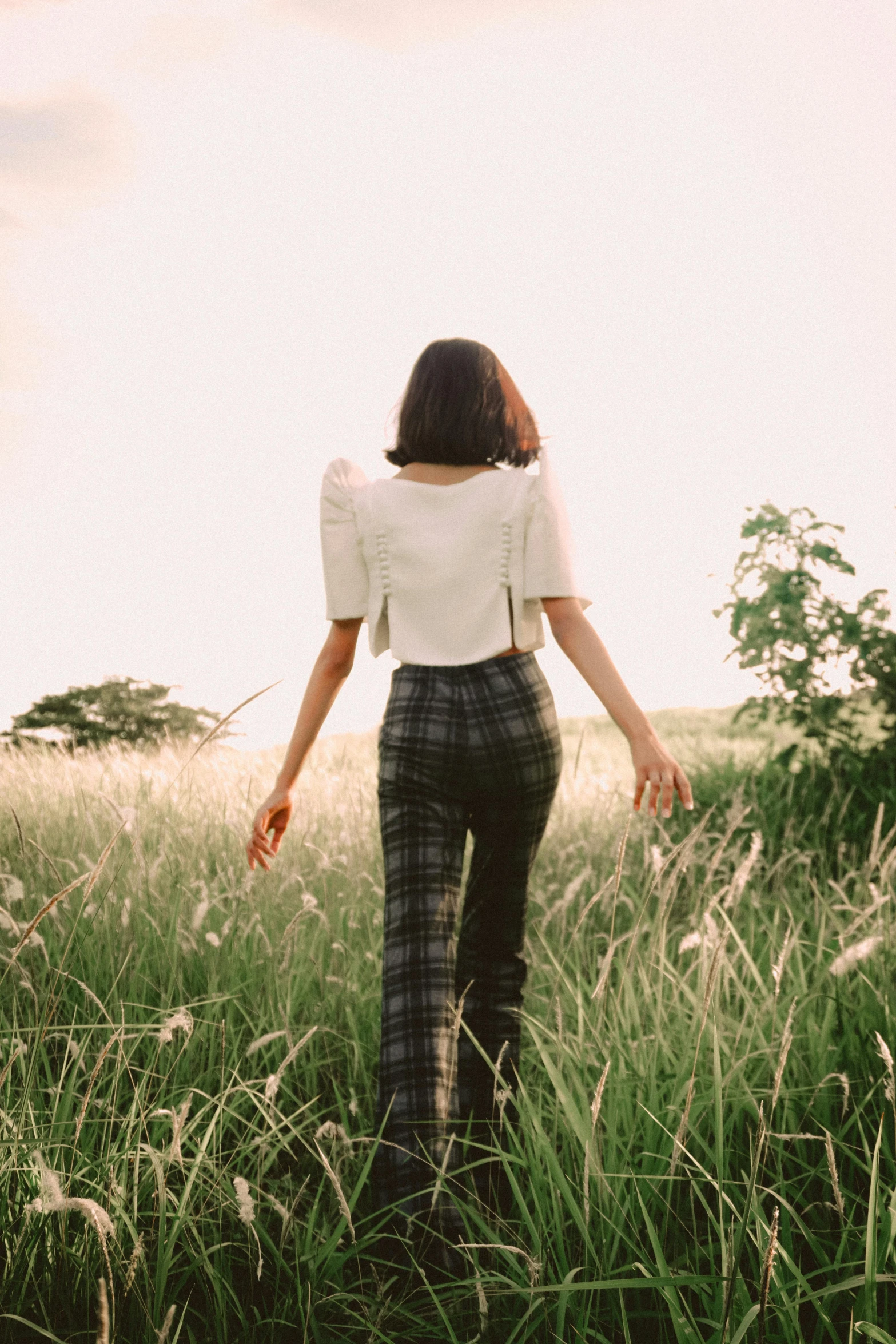 a woman walking through tall grass with her hands in the air