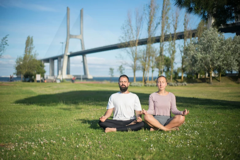 two people in yoga position with a large bridge behind them