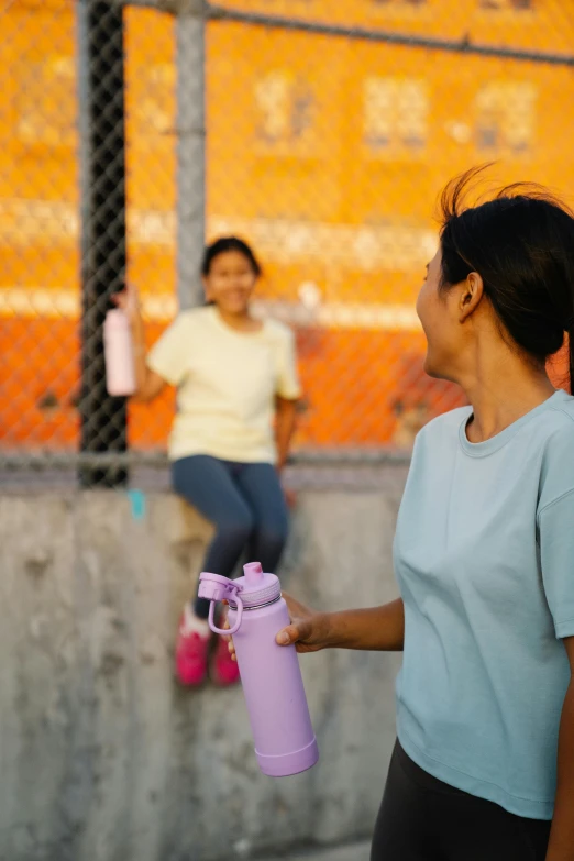 a woman carrying a small purple tube is smiling at a girl who is holding a pink umbrella