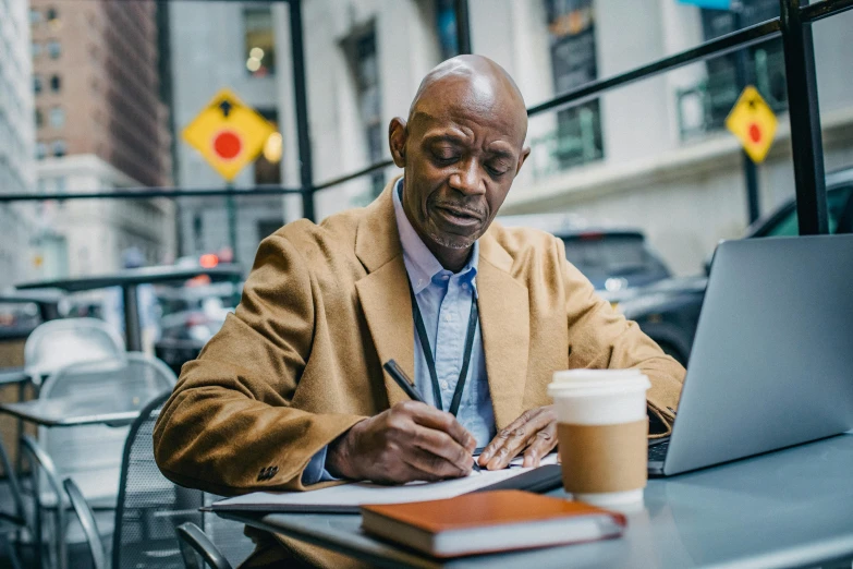 an old man is sitting in a cafe, writing on his workbook