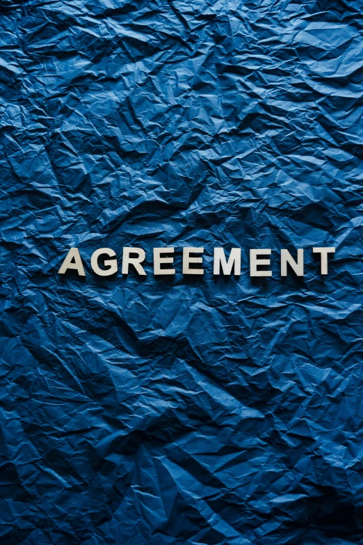 an up close s of a blue crumpled paper with a wooden word that says agreement