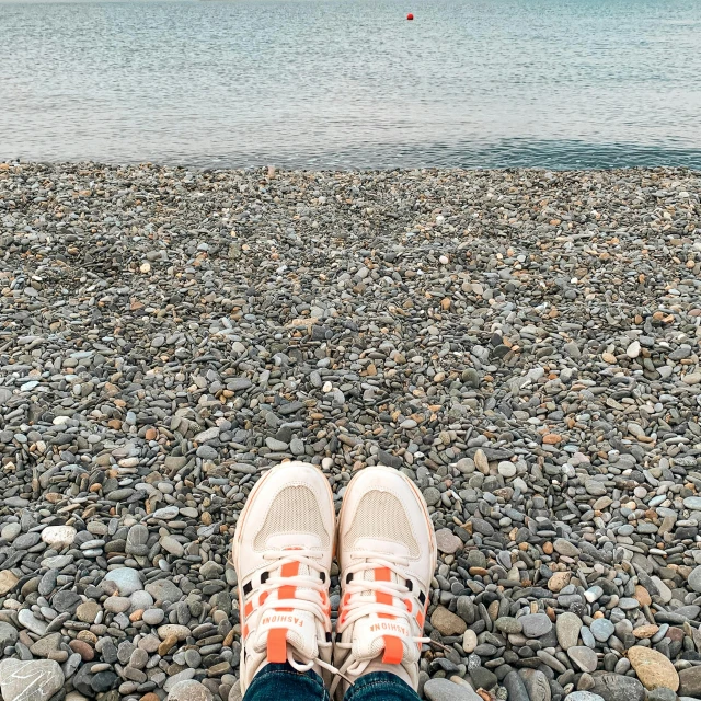 a person's feet propped up on a pebble beach, overlooking the ocean