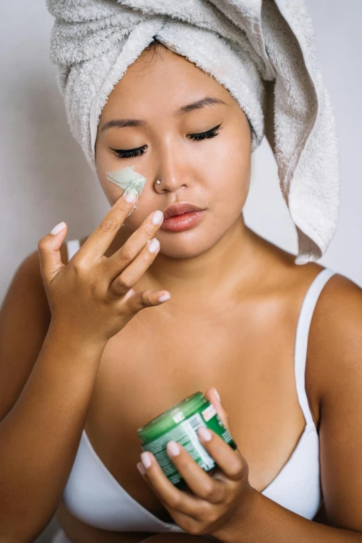 a woman is getting her face cream done with her hand and holding a jar