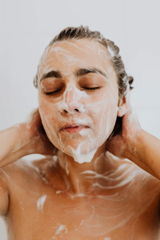 a shirtless young man washing his face with a foamy mask