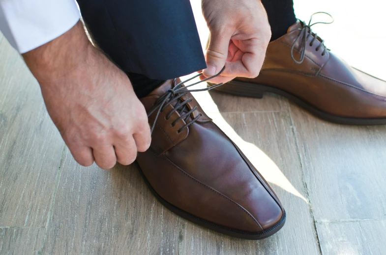 a man tying up a brown derby shoe on the ground