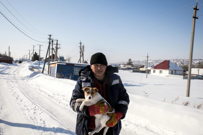 a man with a black hat holding his dog in the snow