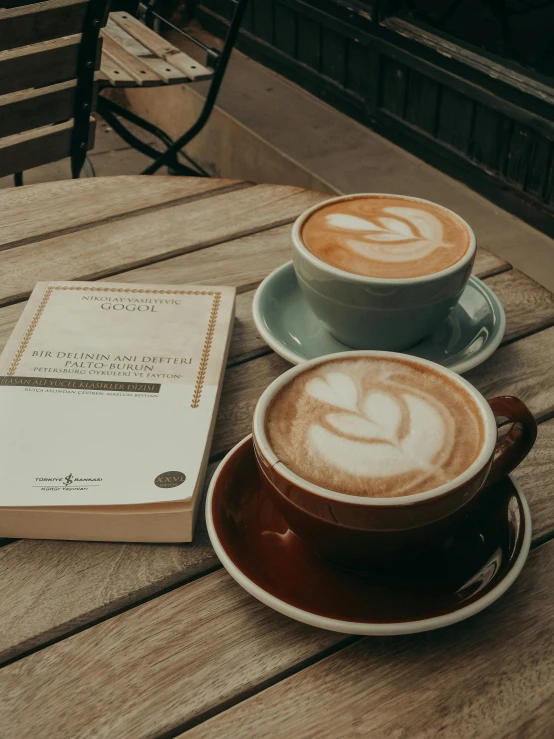 two cups of coffee sitting next to a book