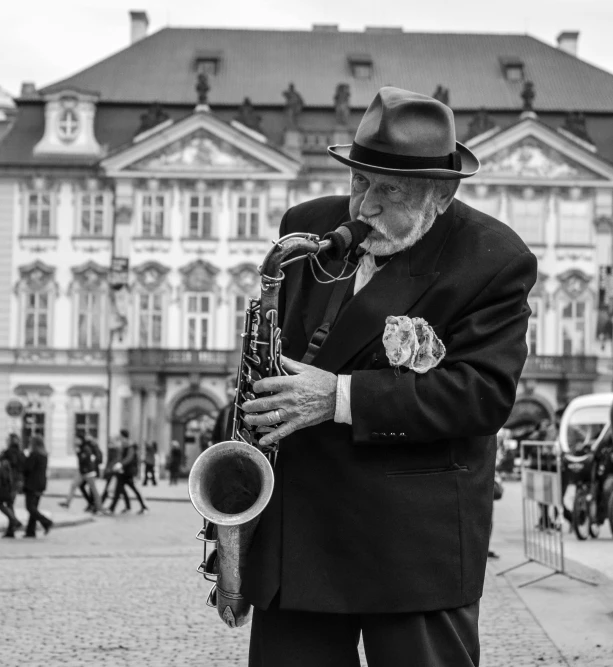 a man with hat and coat playing saxophone in front of an old building