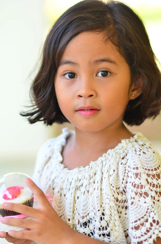 the small girl holds up her cupcake in front of her