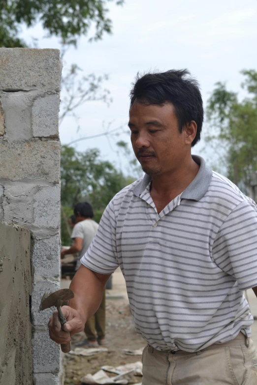 a man in a gray and white shirt holding onto a brick wall