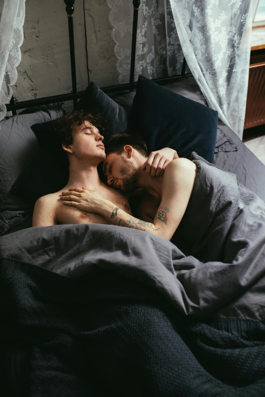 two shirtless men cuddling each other in a bed