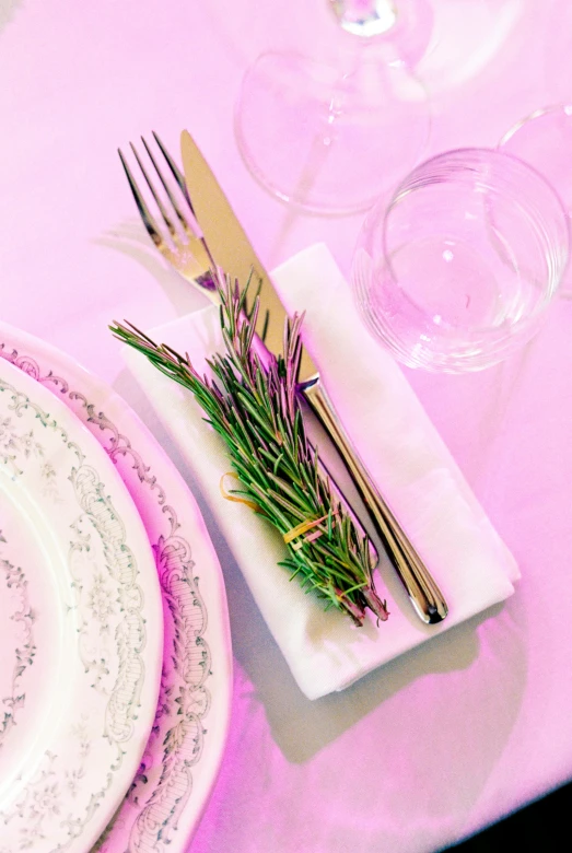 a white table with silverware, two place settings and a pink centerpiece