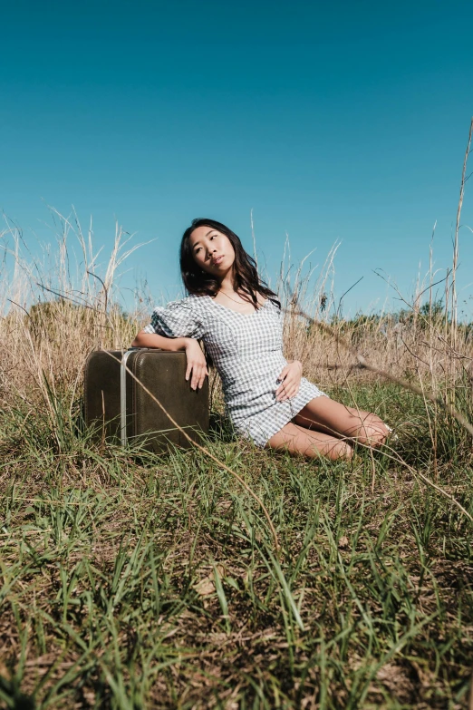 a woman is sitting on a suitcase in a field