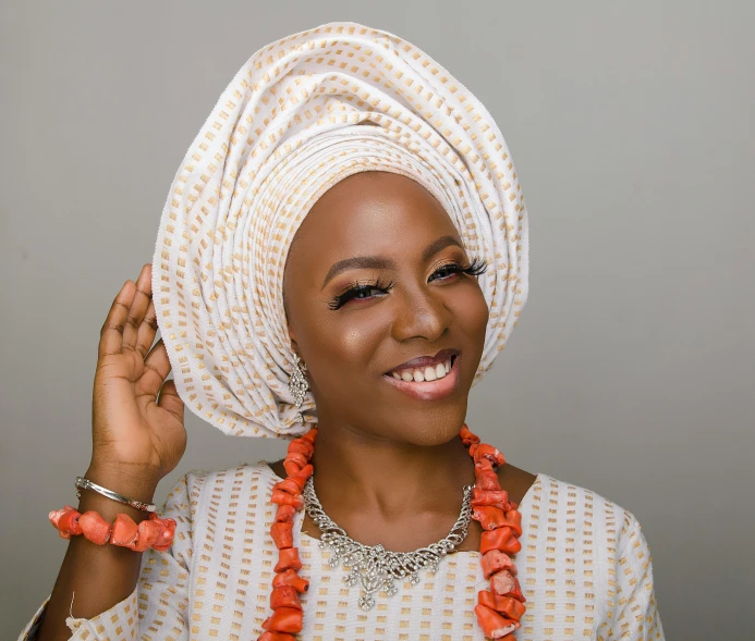 a woman smiling while wearing a hat and orange necklace