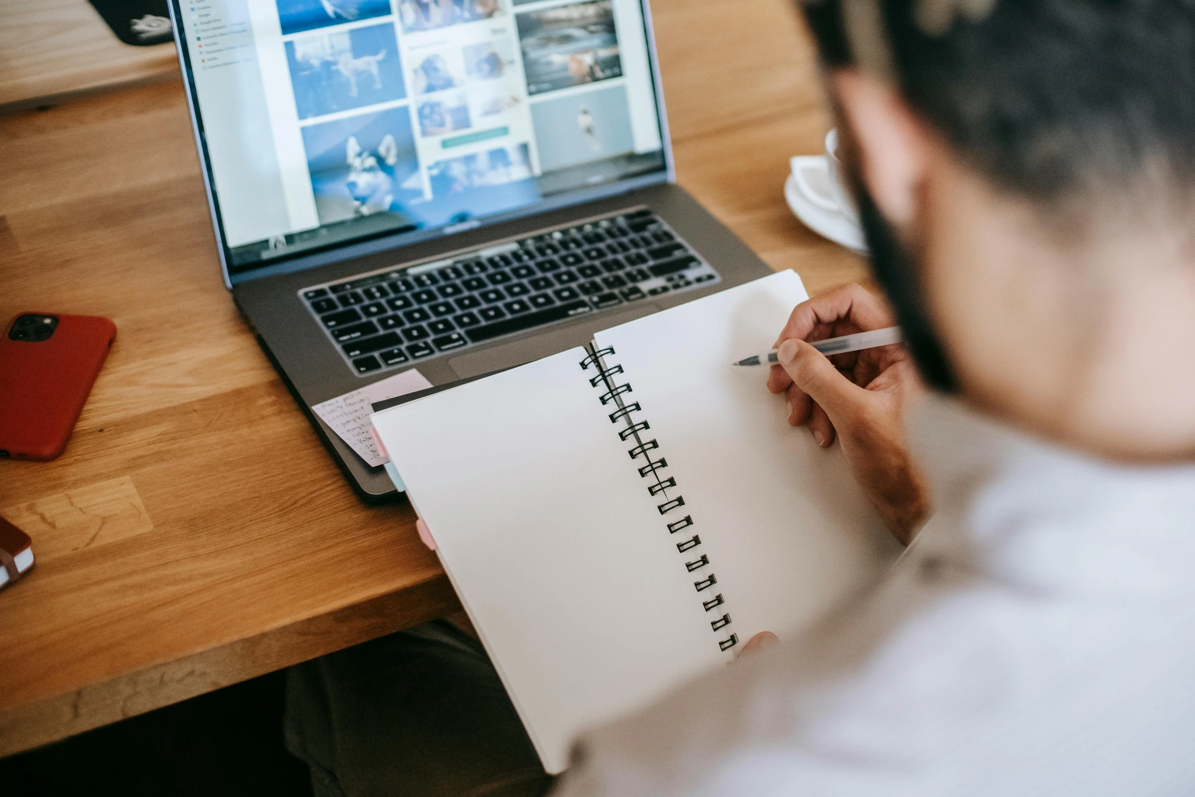 man writing in a notebook on top of a laptop computer