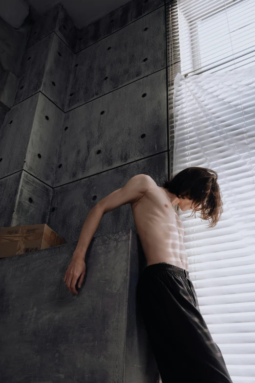 a young man leaning on a wall near a window