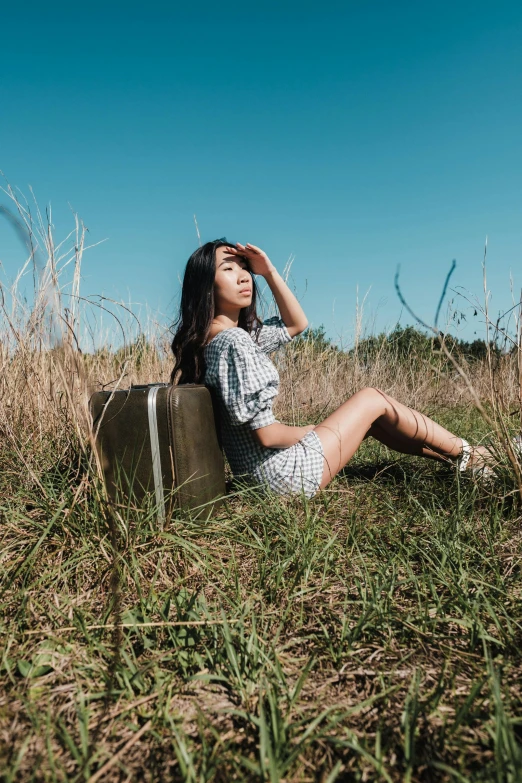 a woman sits in the grass holding her head while looking at the sky