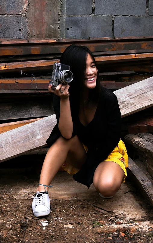 a woman kneeling next to a pile of logs and holding a camera