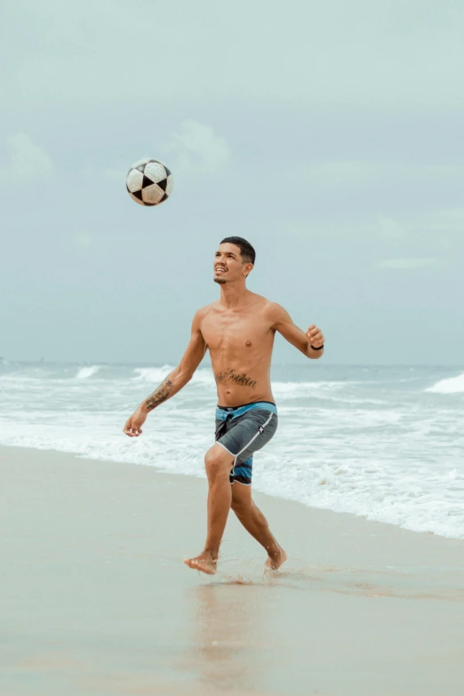 a man playing soccer on the beach on a cloudy day