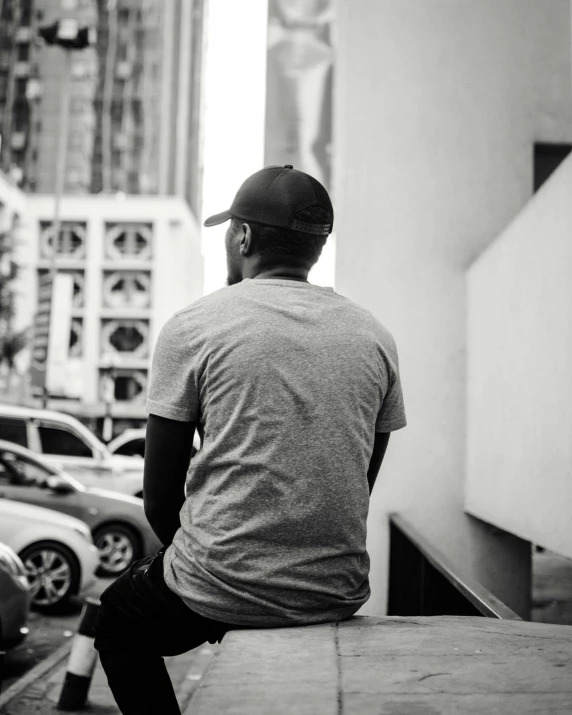 black and white pograph of a man sitting on ledge watching cars