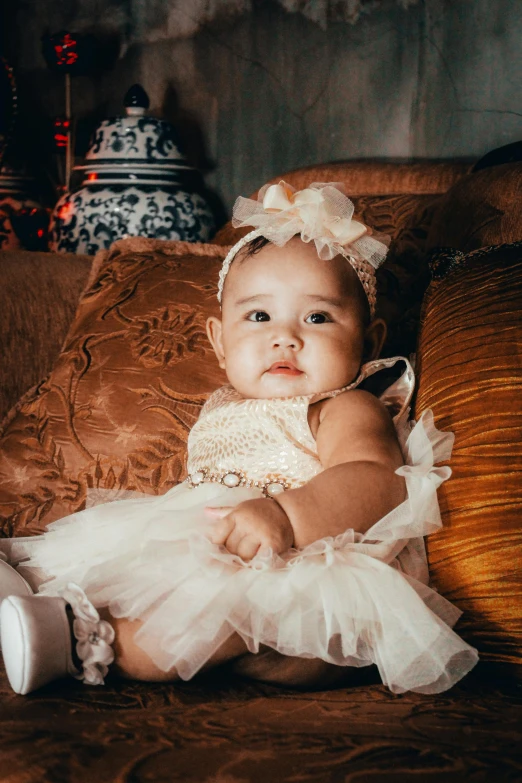a young baby sitting on a couch dressed up in white