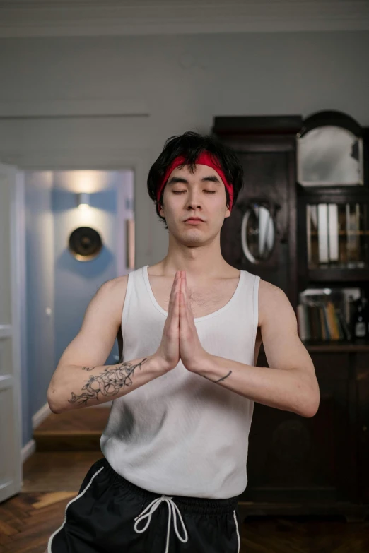 a man with black hair wearing a tank top doing yoga