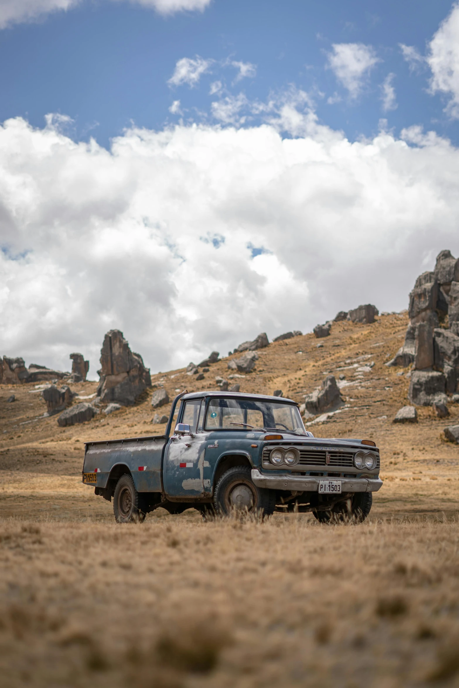 a blue pick up truck driving past rocks in an open field