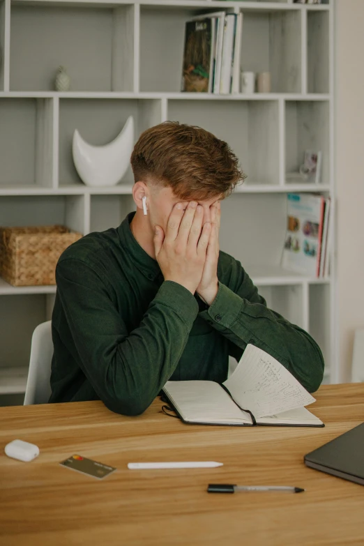 a man sitting at a table while covering his face