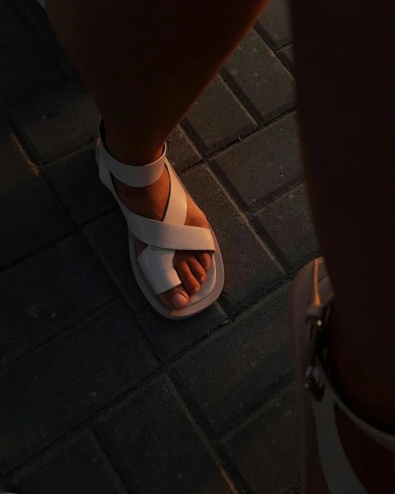 a woman's feet in white sandals standing on brick sidewalk