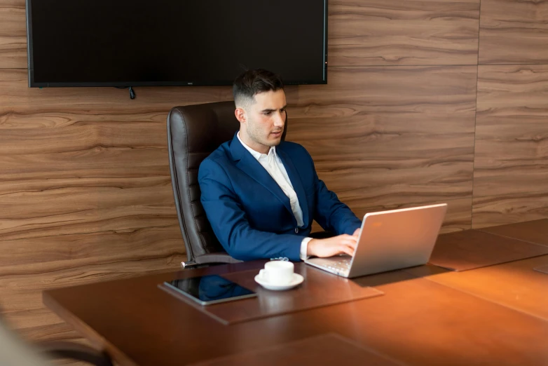 a man sitting in front of a desk working on a laptop