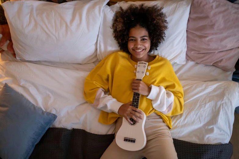 a girl holding a guitar in her hand in front of pillows