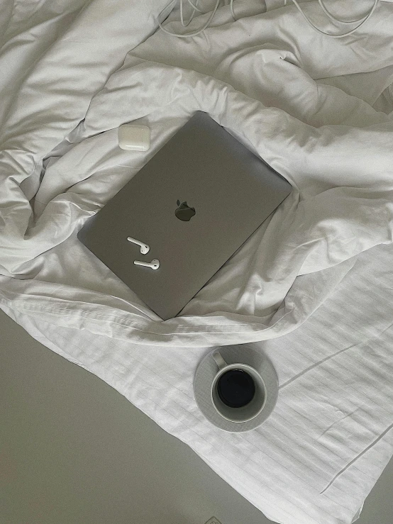 a apple laptop sitting on a bed with a cup and remote control