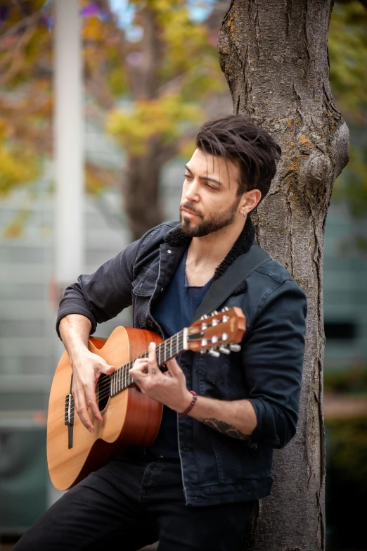 a man holding an acoustic guitar next to a tree