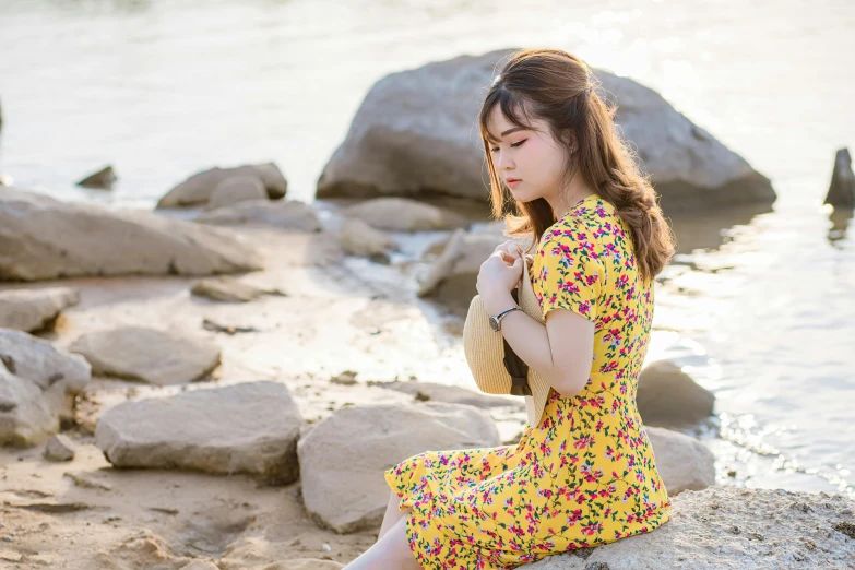 an asian woman sitting on some rocks near a body of water