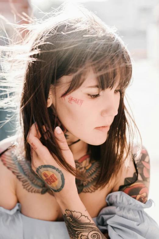 woman with tattoos, holding her hands on her ears