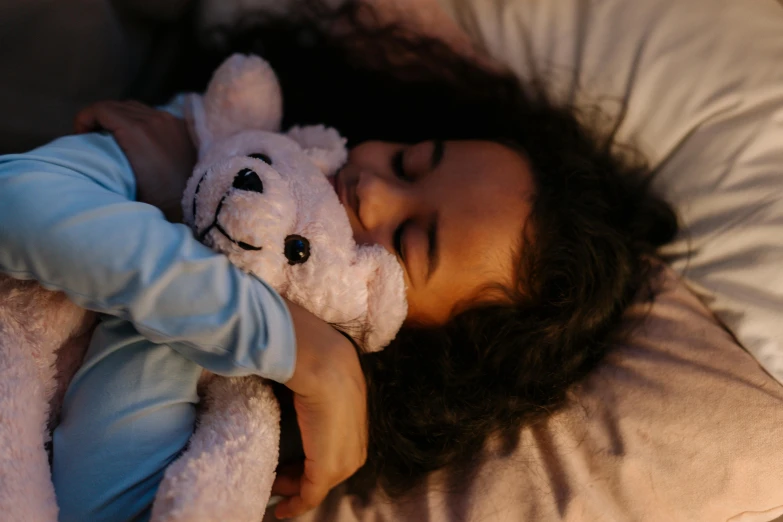 a little girl is laying down on the bed with her stuffed animal