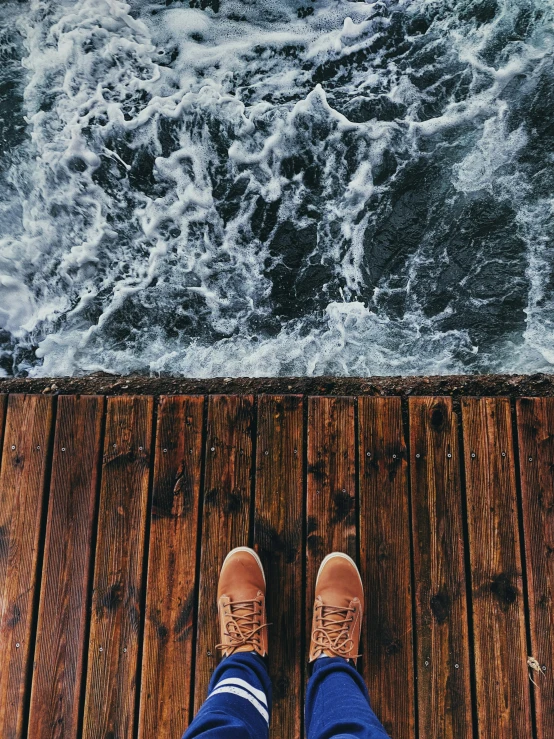 legs in blue pants standing on a wood walkway next to rough water