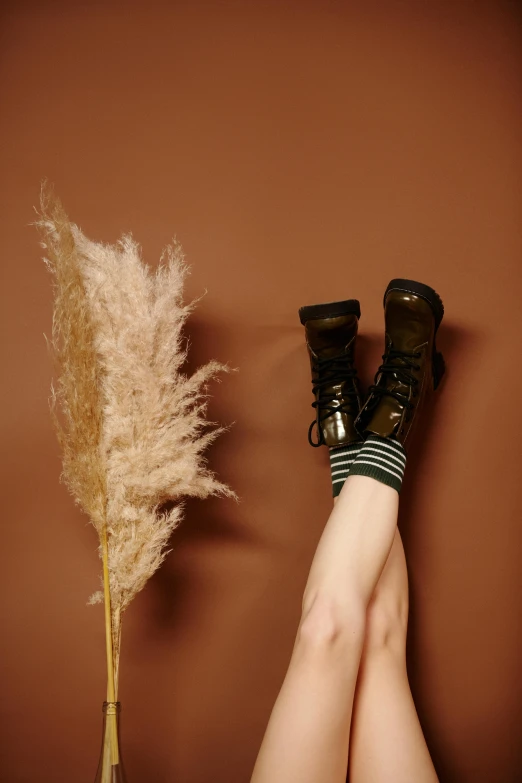 a woman in boots sits next to a tall pamylum and a vase with brown stems